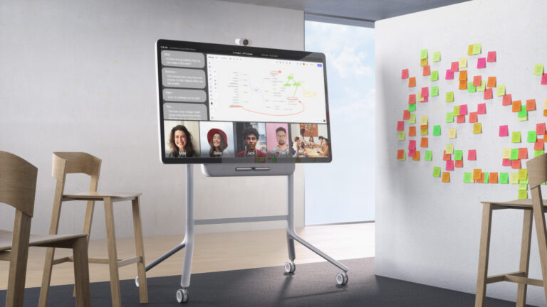 A sleek, high-performance touch display in a collaborative workspace shows a video conference and presentation.